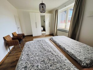 Ein Schlafzimmer mit zwei Betten, einem Kleiderschrank, einem Sessel und einer Pendelleuchte.