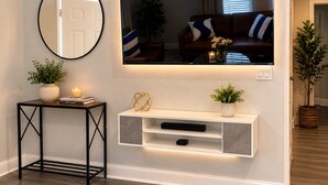 A living room with a mounted TV, a console table with decorative items, a potted plant, and a mirror on the wall.