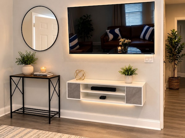 A living room with a mounted TV, a console table with decorative items, a potted plant, and a mirror on the wall.