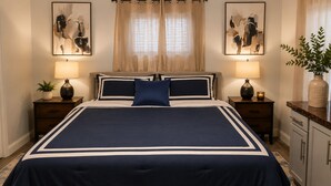 A large bed with a navy blue and white bedspread, flanked by two bedside tables with lamps, a potted plant, and artwork on the walls. - Spacious, Quiet 1BR close to downtown, Medical Center, NRG & UH. Pet Ok. (Houston)