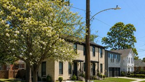 A residential street with houses, a sidewalk, and a tree with white blossoms.
