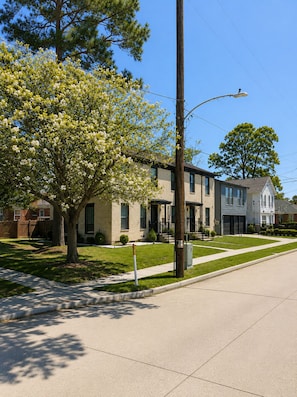 A residential street with houses, a sidewalk, and a tree with white blossoms.