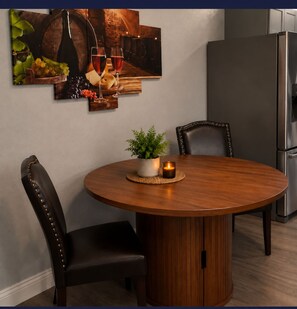 A round wooden dining table with chairs, a potted plant, and a candle on a placemat.