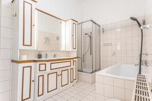 A bathroom with a white tiled floor, a large mirror, a glass-enclosed shower, and a white bathtub.