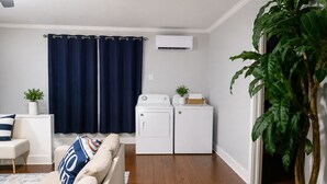 A modern living room with a sofa, a large potted plant, a ceiling fan, and a laundry area with two washing machines.