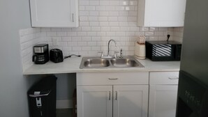 A small kitchen with white cabinets, a double sink, a coffee maker, a toaster, and a microwave.