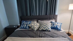 A bed with a grey quilt, two pillows with 'LOVE' and 'HOME' text, a dark headboard, and a bedside table.