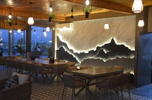 Ein Restaurant mit Holztischen, hängenden Lampen und einer Wand mit Bergmotiv.