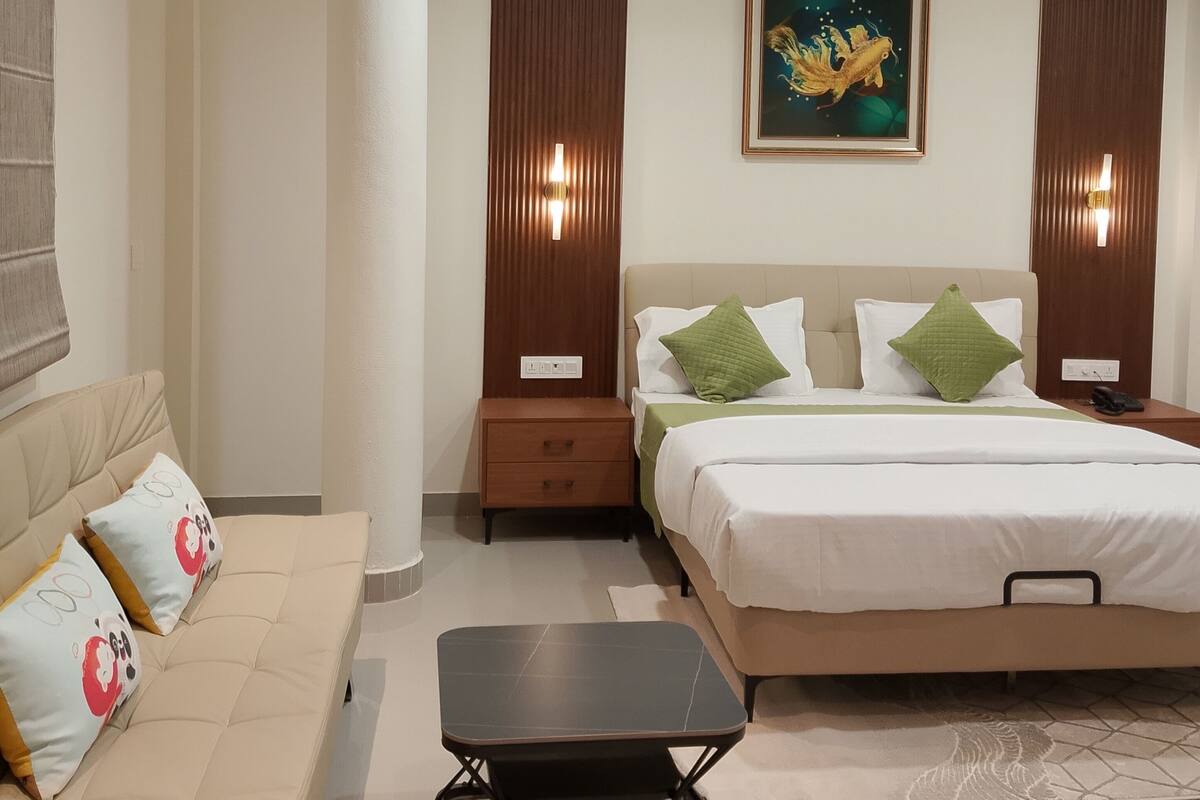 Moderni hotellihuone, jossa on sänky, sohva, pieni pöytä ja kattotuuletin.
