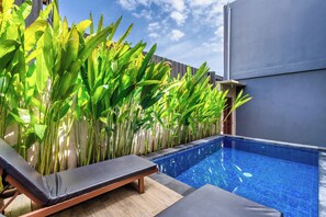A swimming pool with a tiled edge, surrounded by lounge chairs and tall green plants. - Rumah Kodel Legian (Legian)