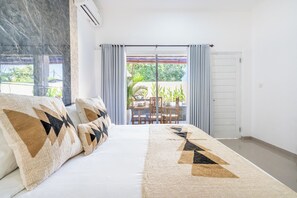 A bedroom with a bed, curtains, and a view of an outdoor patio with a table and chairs. - Rumah Kodel Legian (Legian)