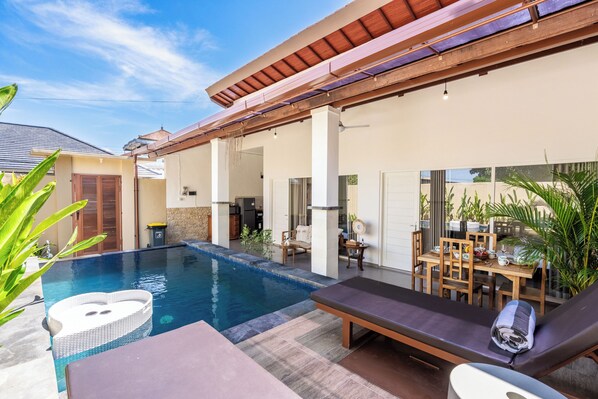 A poolside area with lounge chairs, a table, and a dining set. - Rumah Kodel Legian (Legian)