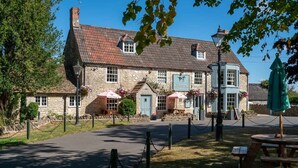 Un bâtiment en pierre à l’architecture traditionnelle, avec une enseigne de pub, des tables à l’extérieur et une pelouse bien entretenue.