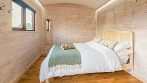 Une pièce aux murs lambrés, avec un lit, une fenêtre et une petite étagère.