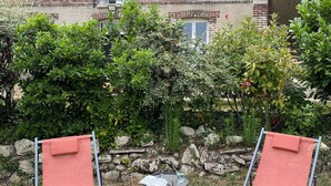 Two outdoor chairs with a table and a book, set against a brick building with a stone wall and greenery. - Large 4* gîte: sleeps 12, 6 bedrooms, 4 bathrooms, games room, garden (Laon)