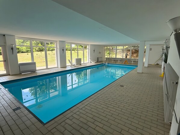 An indoor swimming pool with clear views of a grassy area outside through large windows. - Apartment Schwarzwald Heimat with Terrace, Pool, Sauna, and Fitness (Schönwald)