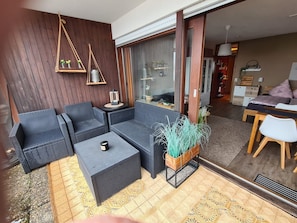 A modern living area with wicker furniture, a wooden wall, and a large sliding glass door leading to a bedroom.