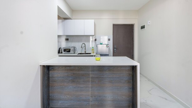 A compact kitchen with white cabinets, a microwave, a kettle, and a refrigerator. - Yaya Suites (Nairobi)