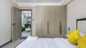 A hotel room with a large bed, a wardrobe, and a view into the hallway. - Yaya Suites (Nairobi)