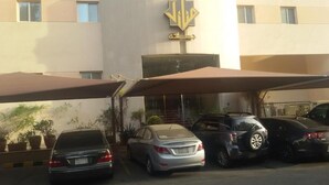 A parking area with several cars, a building with a logo, and potted plants. - MANAZIL JEDDAH for Serviced Apartment (Jeddah)