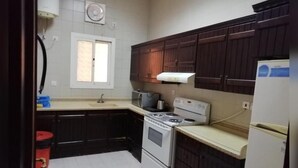 A kitchen with dark wooden cabinets, a white stove, and a white refrigerator. - MANAZIL JEDDAH for Serviced Apartment (Jeddah)