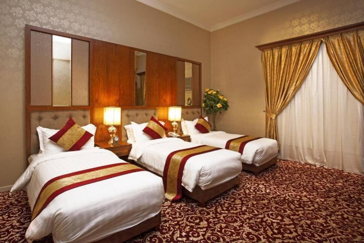 Une chambre d’hôtel avec trois lits, un grand miroir et une moquette rouge.
