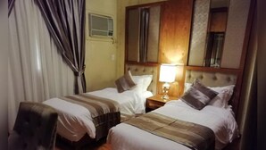 A hotel room with two beds, a wooden headboard, a nightstand with a lamp, and a chair. - MANAZIL JEDDAH for Serviced Apartment (Jeddah)