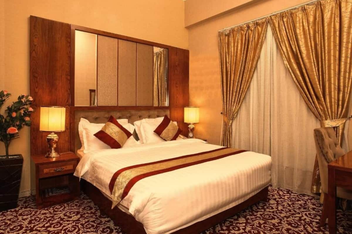 Une chambre d’hôtel avec un grand lit, deux tables de chevet avec des lampes, un miroir au-dessus du lit et une fenêtre avec des rideaux.