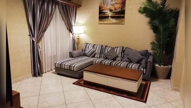 A living room with a sofa, a coffee table, a lamp, a painting, and a potted plant. - MANAZIL JEDDAH for Serviced Apartment (Jeddah)