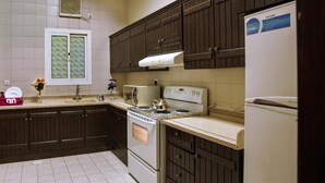 A kitchen with dark wooden cabinets, a white stove, and a white refrigerator. - MANAZIL JEDDAH for Serviced Apartment (Jeddah)