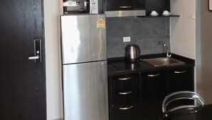 A compact kitchen with a refrigerator, microwave, stove, and black cabinets. - Well-located condo 1-BR T1-NV 203 (Chalong)