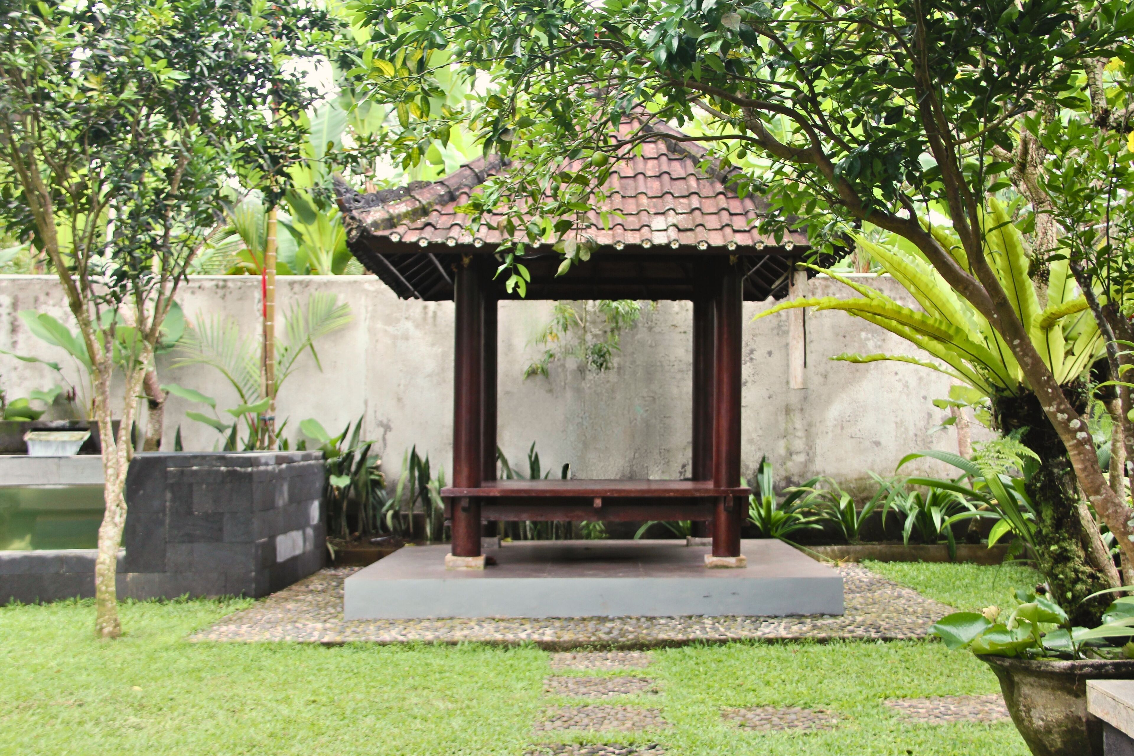 A gazebo with a tiled roof and a bench in a garden setting.