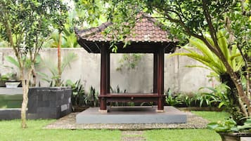 A gazebo with a tiled roof and a bench in a garden setting.