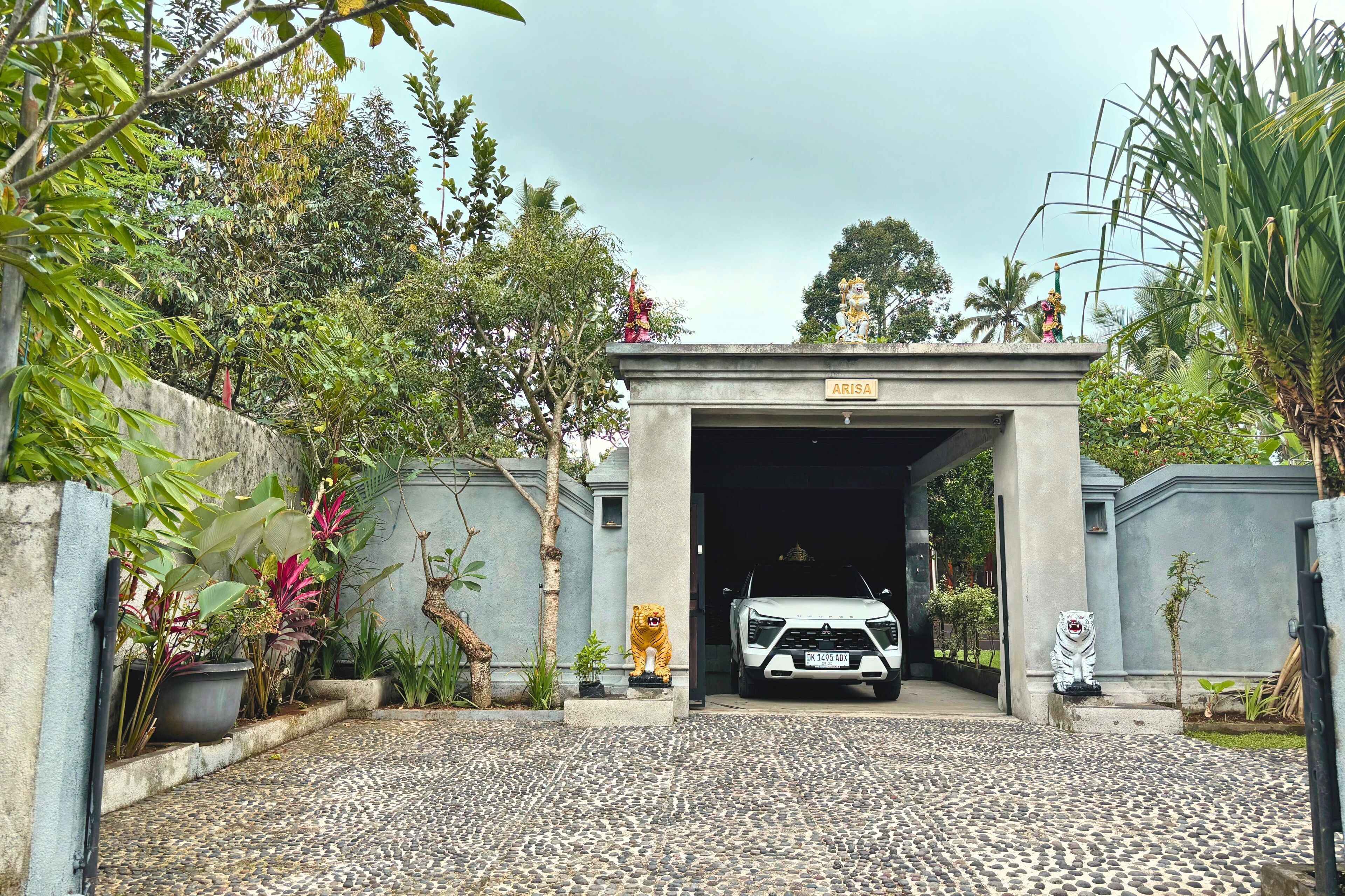 A gated entrance with a sign reading 'ARISA,' a white vehicle parked inside, and a tiger statue on the right.
