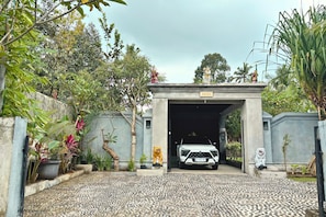Una entrada con reja y un letrero que dice 'ARISA', un vehículo blanco estacionado en el interior y una estatua de tigre a la derecha.