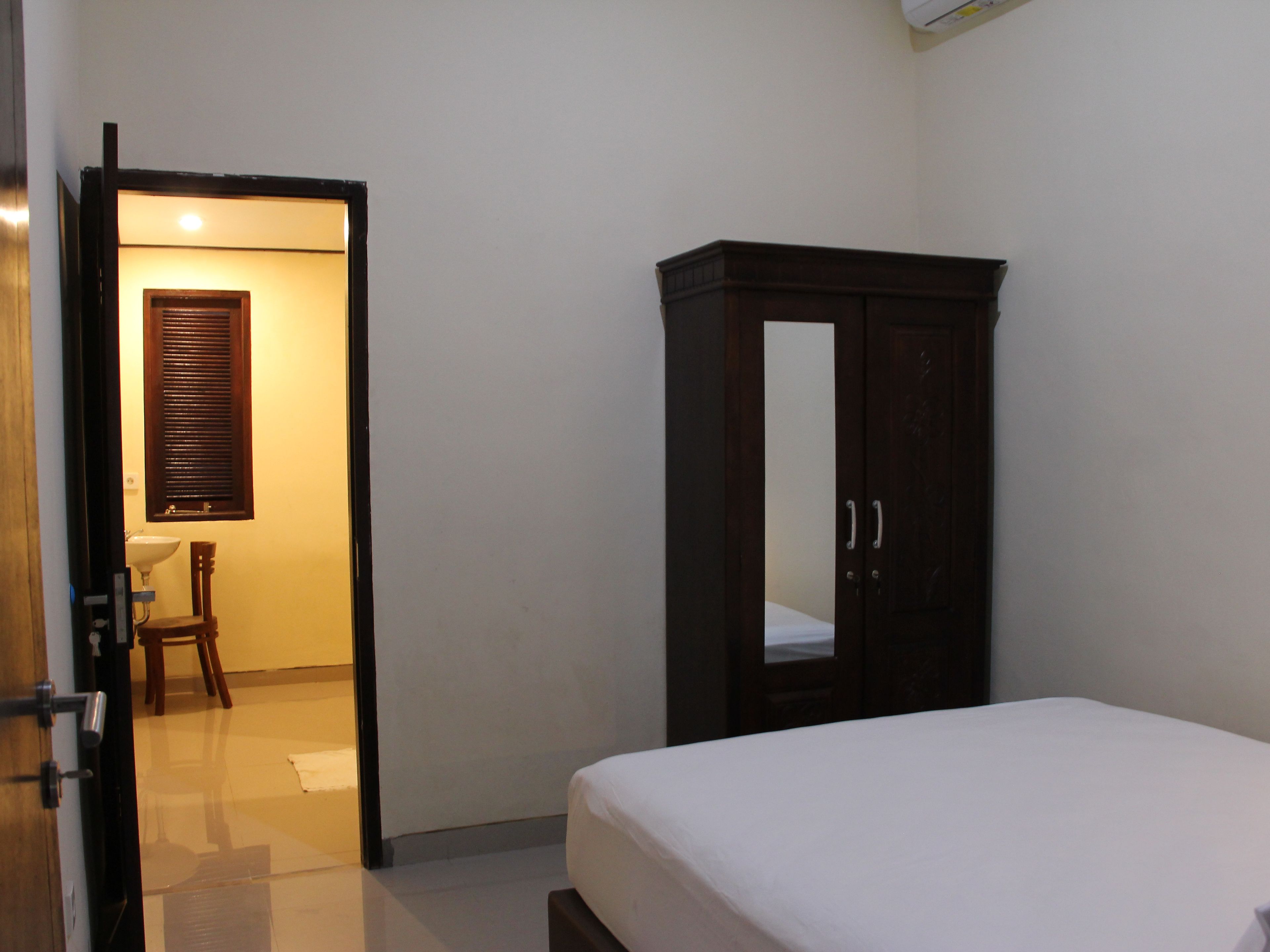 Un dormitorio con cama, armario, puerta que da a un baño y ventana con persianas.