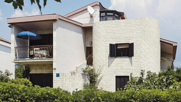 Une maison moderne à deux étages, dotée d’une antenne parabolique, d’un balcon avec un parasol bleu et d’une façade en briques.
