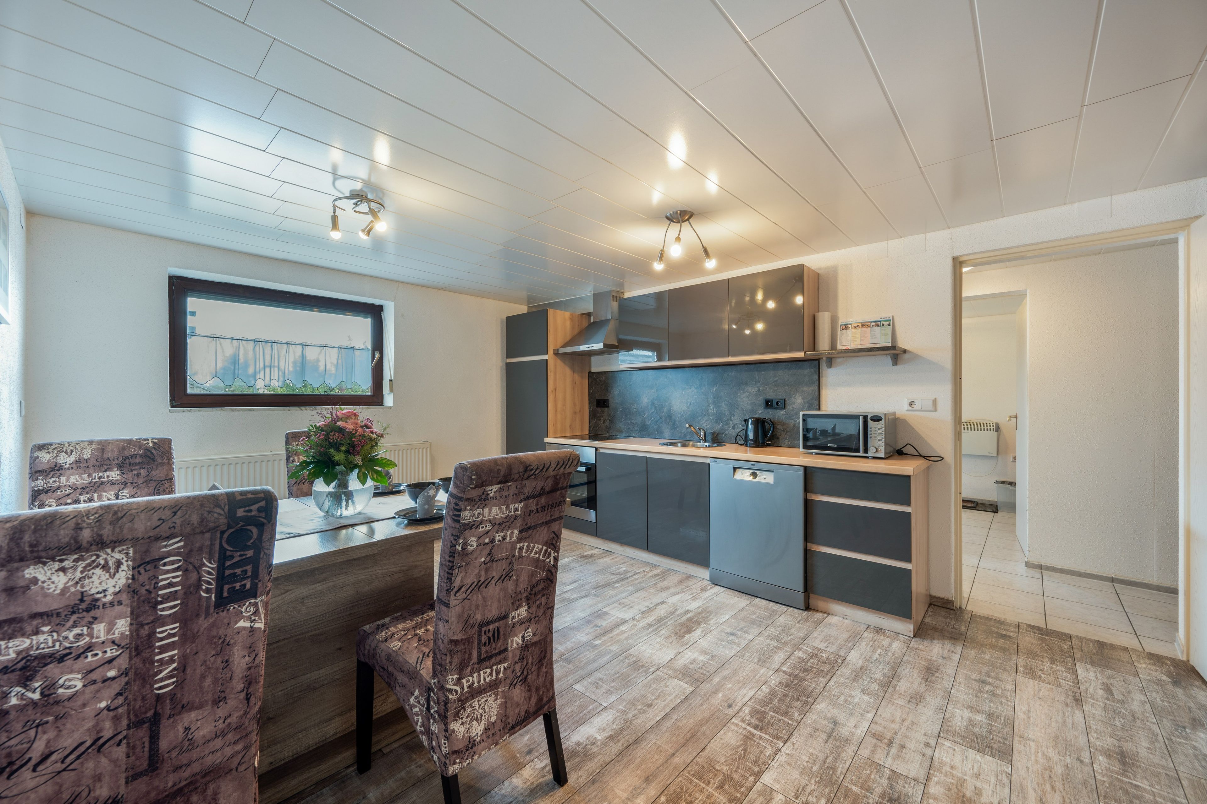 A modern kitchen with a built-in dishwasher, a microwave, and a coffee maker. There is a dining area with a table and chairs.