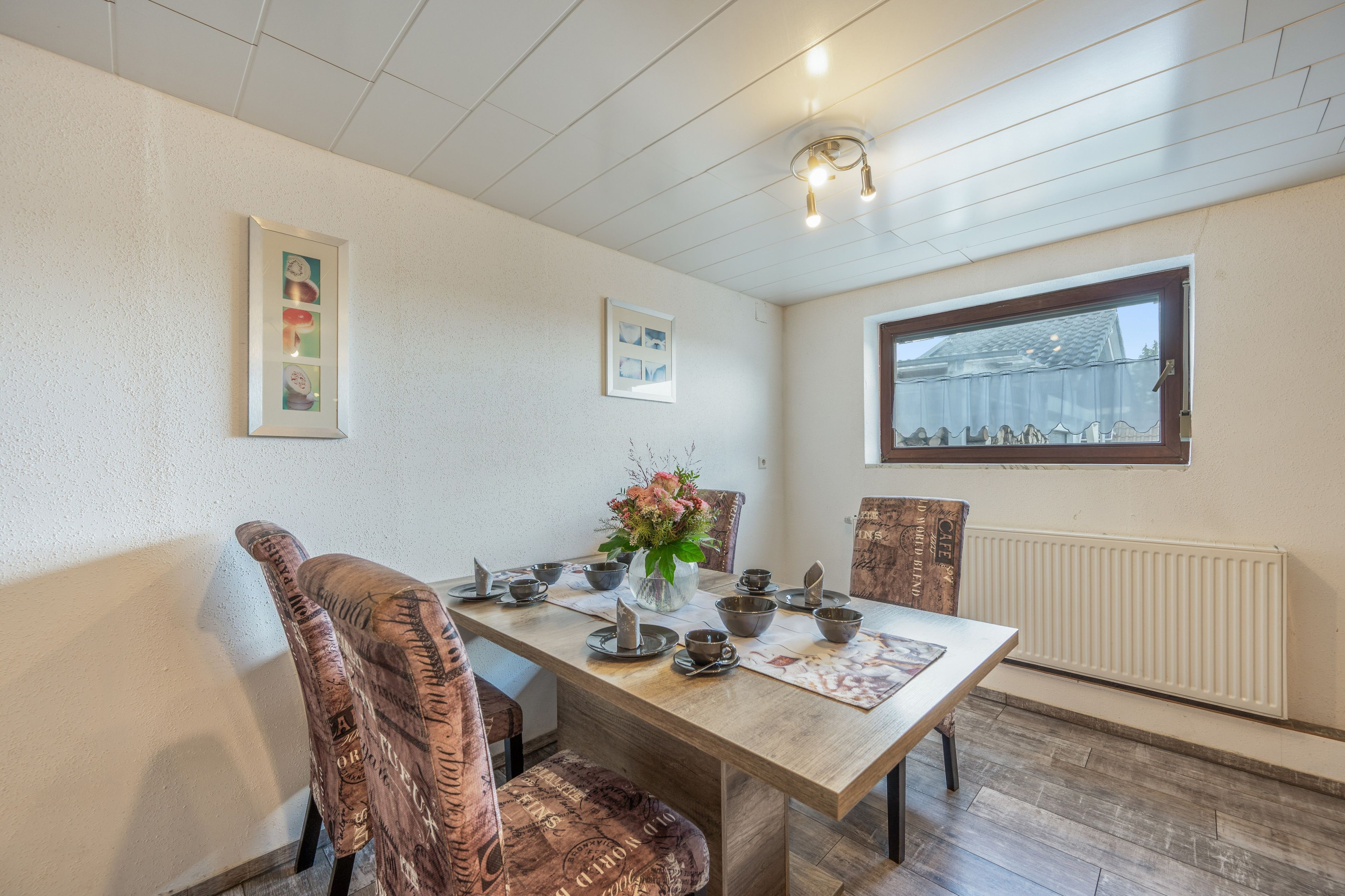 A dining area with a wooden table set for four, a vase with flowers, and a window with a view of a building.