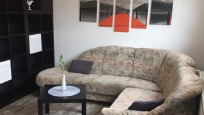 Un salon avec un canapé, une petite table sur laquelle est posé un vase, et une étagère noire.