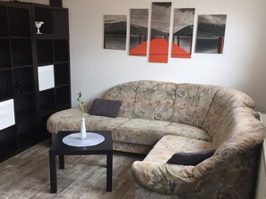 Un salon avec un canapé, une petite table sur laquelle est posé un vase, et une étagère noire.