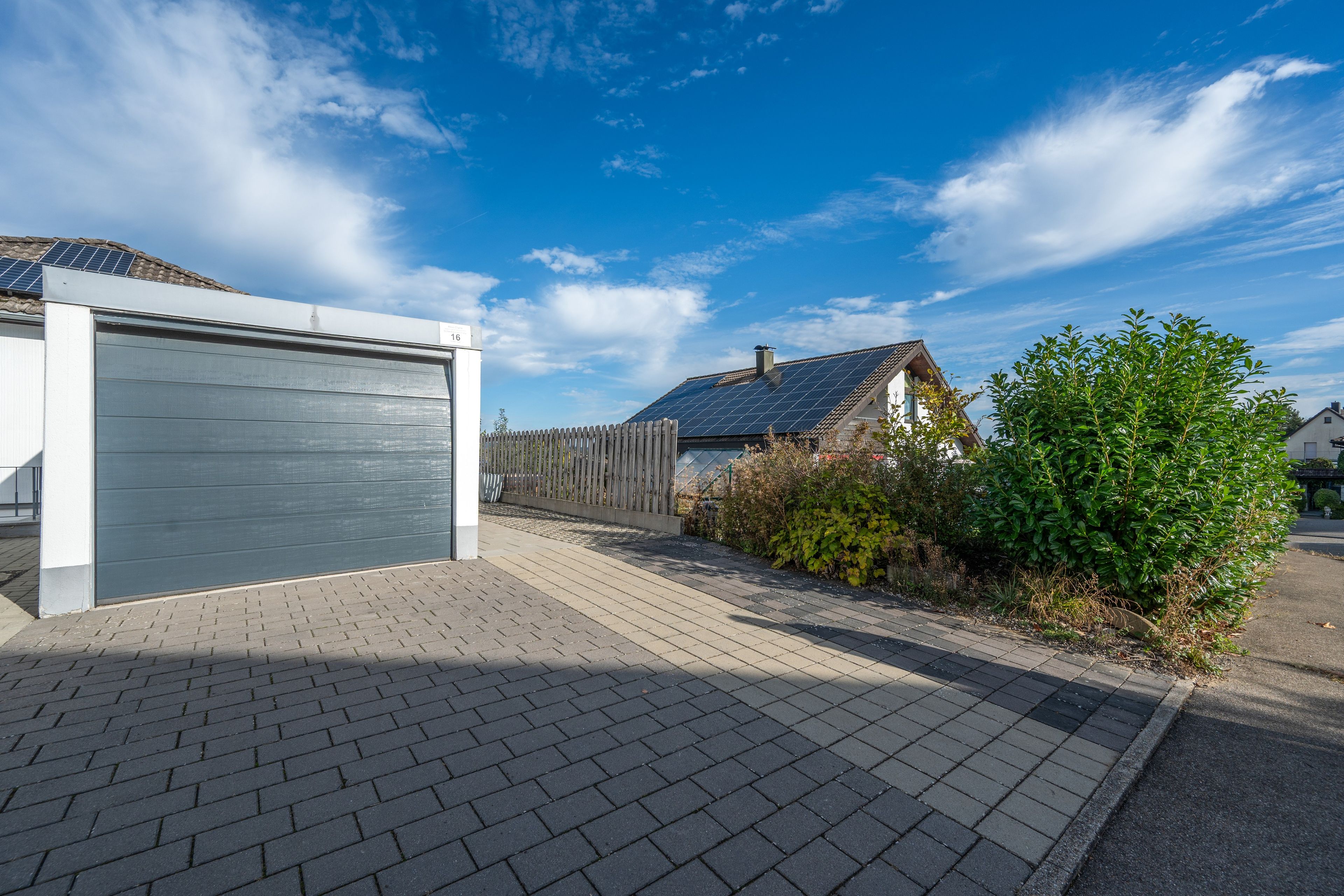 A residential property with a garage, a paved driveway, and a house with solar panels.