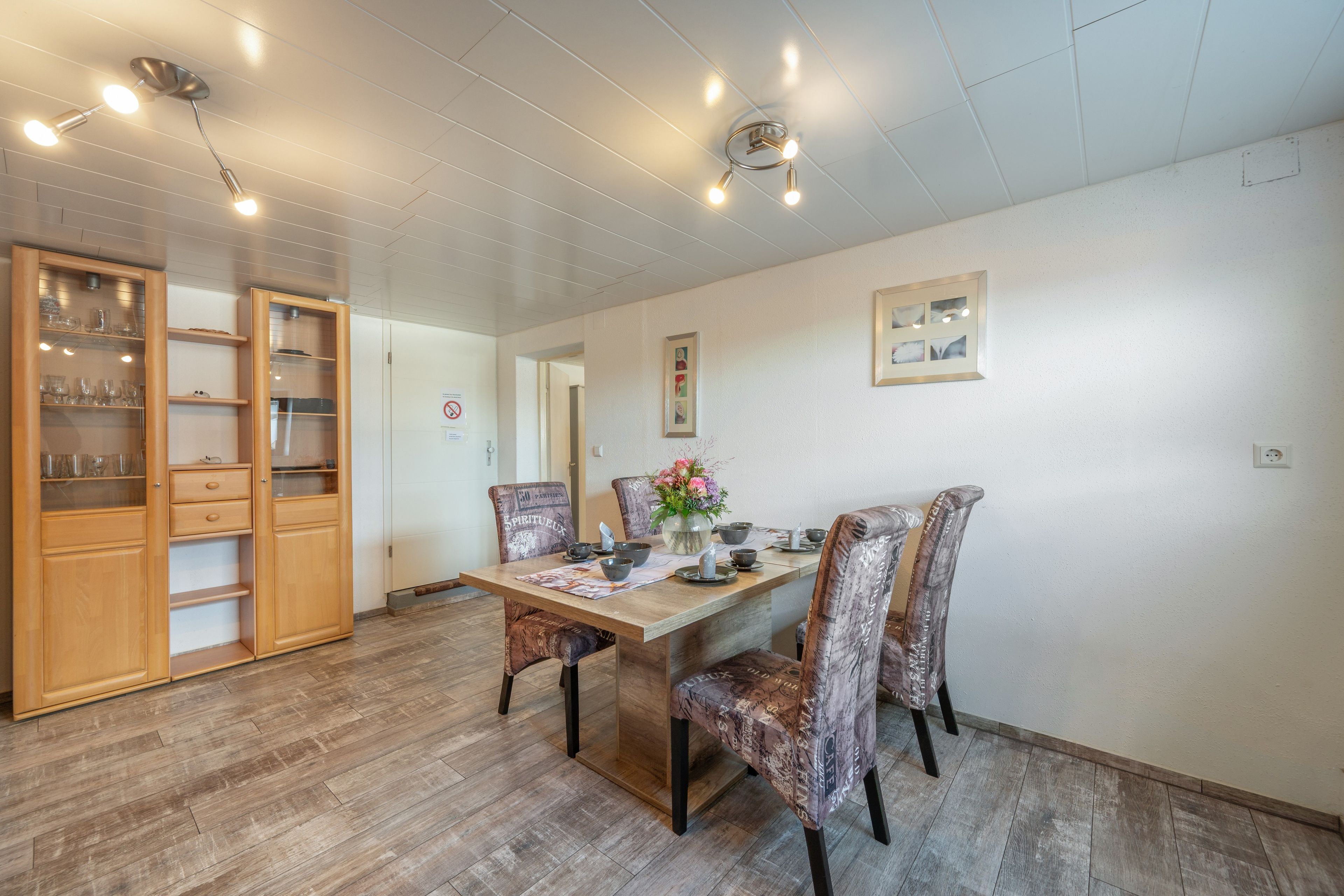 A dining area with a wooden table, chairs, and a cabinet with glassware.