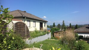 Un immeuble résidentiel doté d’un toit en pente, d’un portail en bois et d’un jardin avec un bassin.