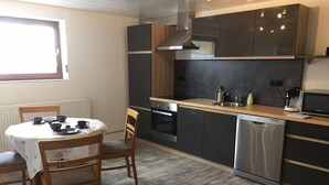 Une cuisine moderne avec une table à manger, des chaises, un four encastré, un lave-vaisselle et une fenêtre.