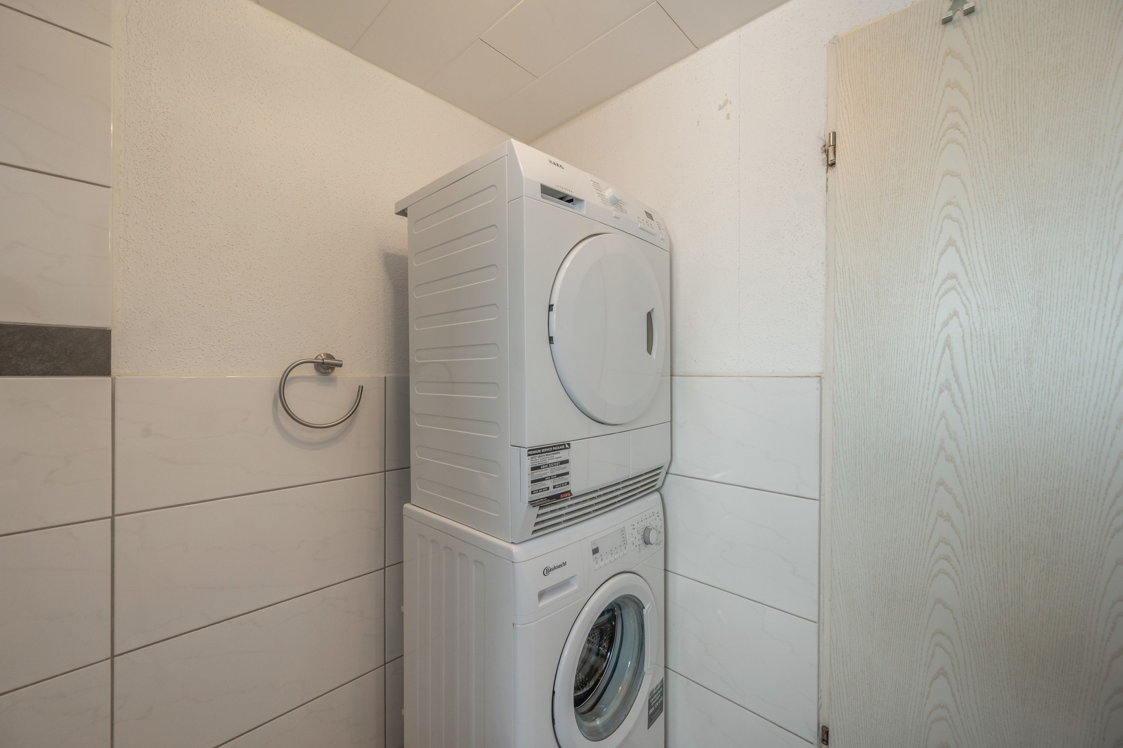 A stacked washer and dryer unit in a bathroom with white tiled walls.