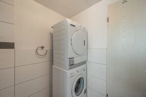 A stacked washer and dryer unit in a bathroom with white tiled walls.