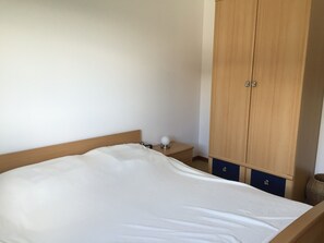 Quarto com cama, mesa de cabeceira, abajur e guarda-roupa.