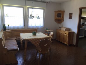 Uma área de refeições com mesa, cadeiras, um banco, um armário de madeira e uma janela com cortinas.