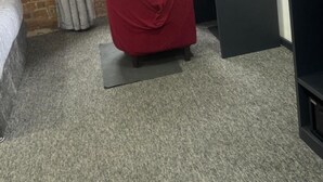 Une pièce comprenant un lit, un fauteuil rouge, un bureau avec un ordinateur, une télévision et une fenêtre avec des rideaux.
